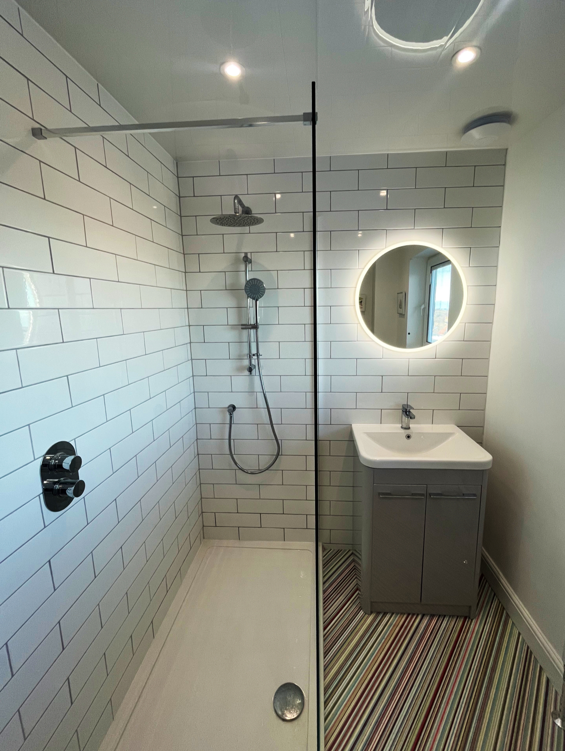 Walk-in shower with white metro tiles, rainfall head and round LED mirror