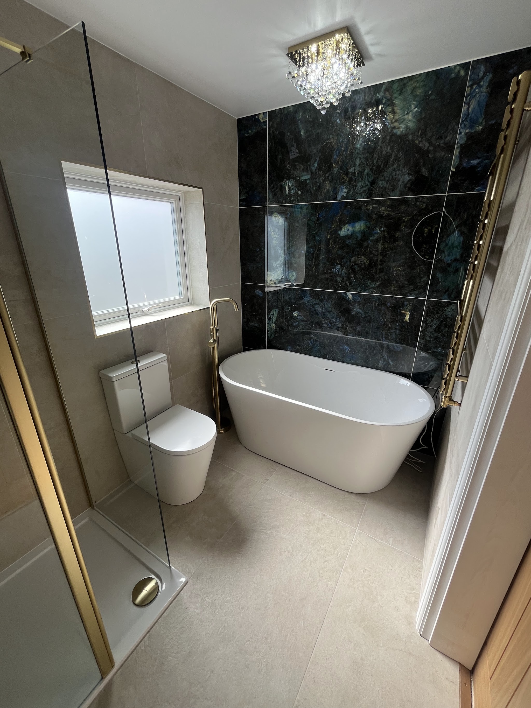 Renovated bathroom with a dark marble-effect feature wall, freestanding bath, brushed gold tap and towel rail