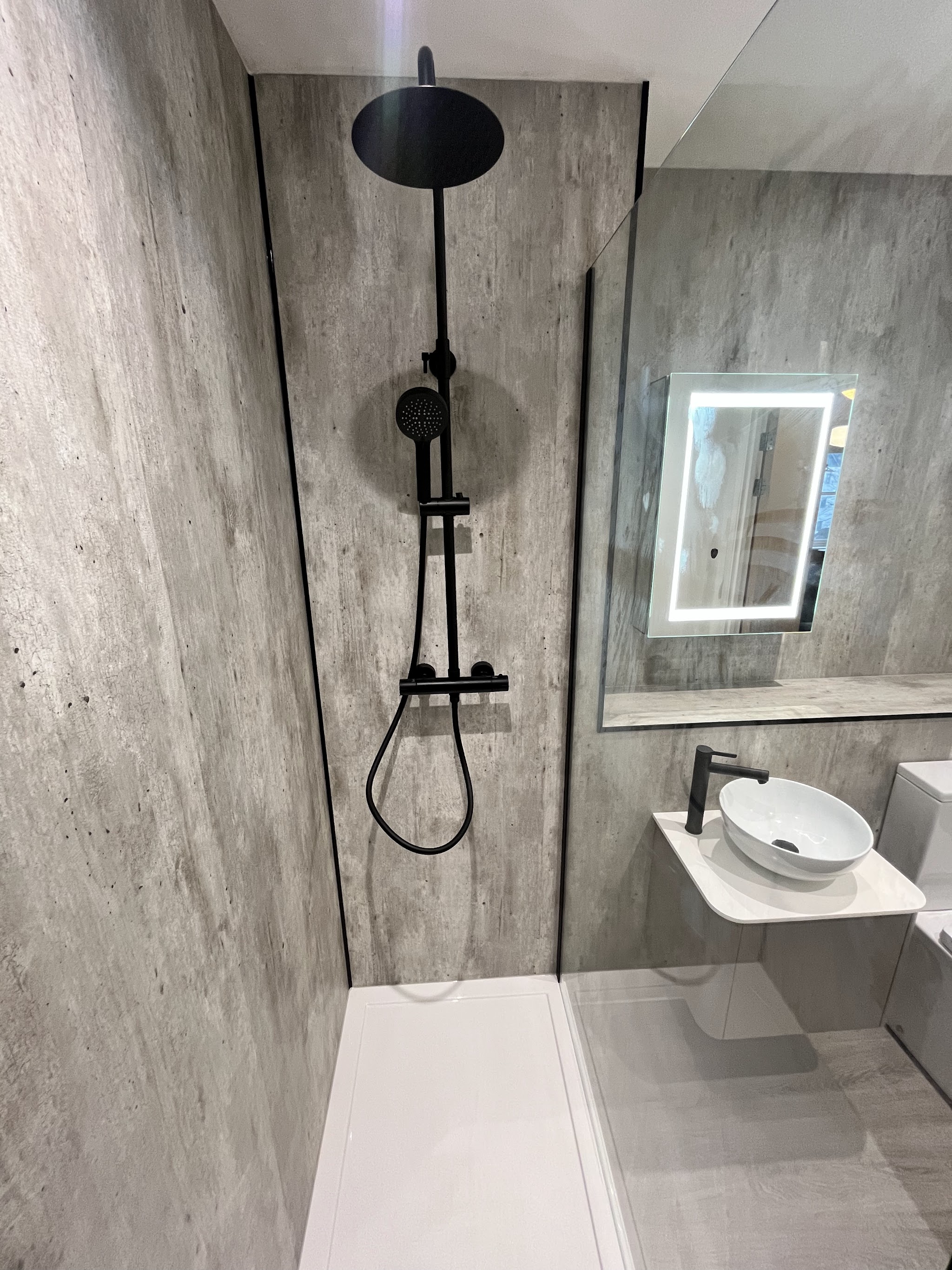 Matt black thermostatic shower with rainfall head against concrete-effect panels