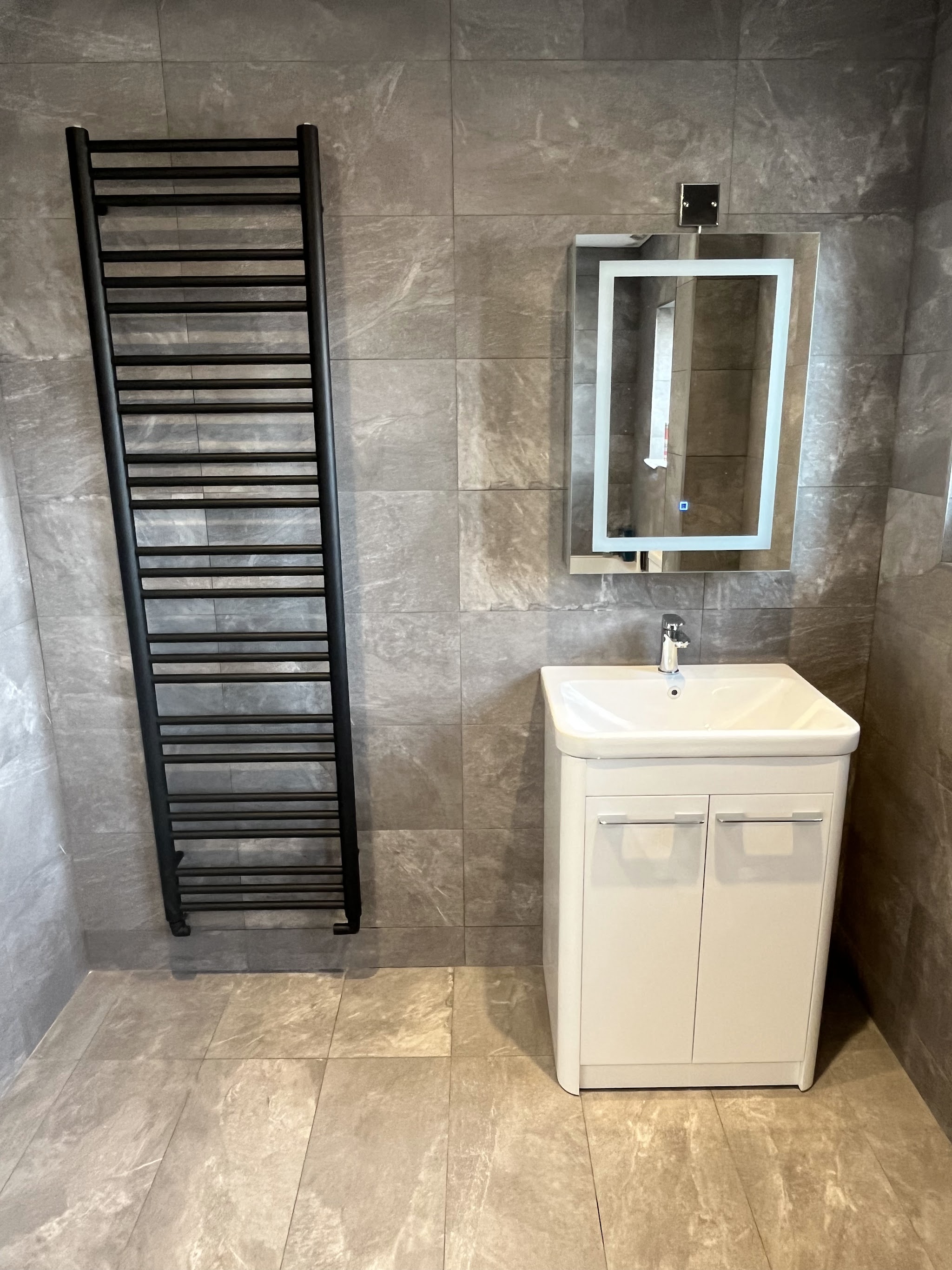 Grey stone-effect tiled bathroom with a tall black towel radiator and white vanity unit