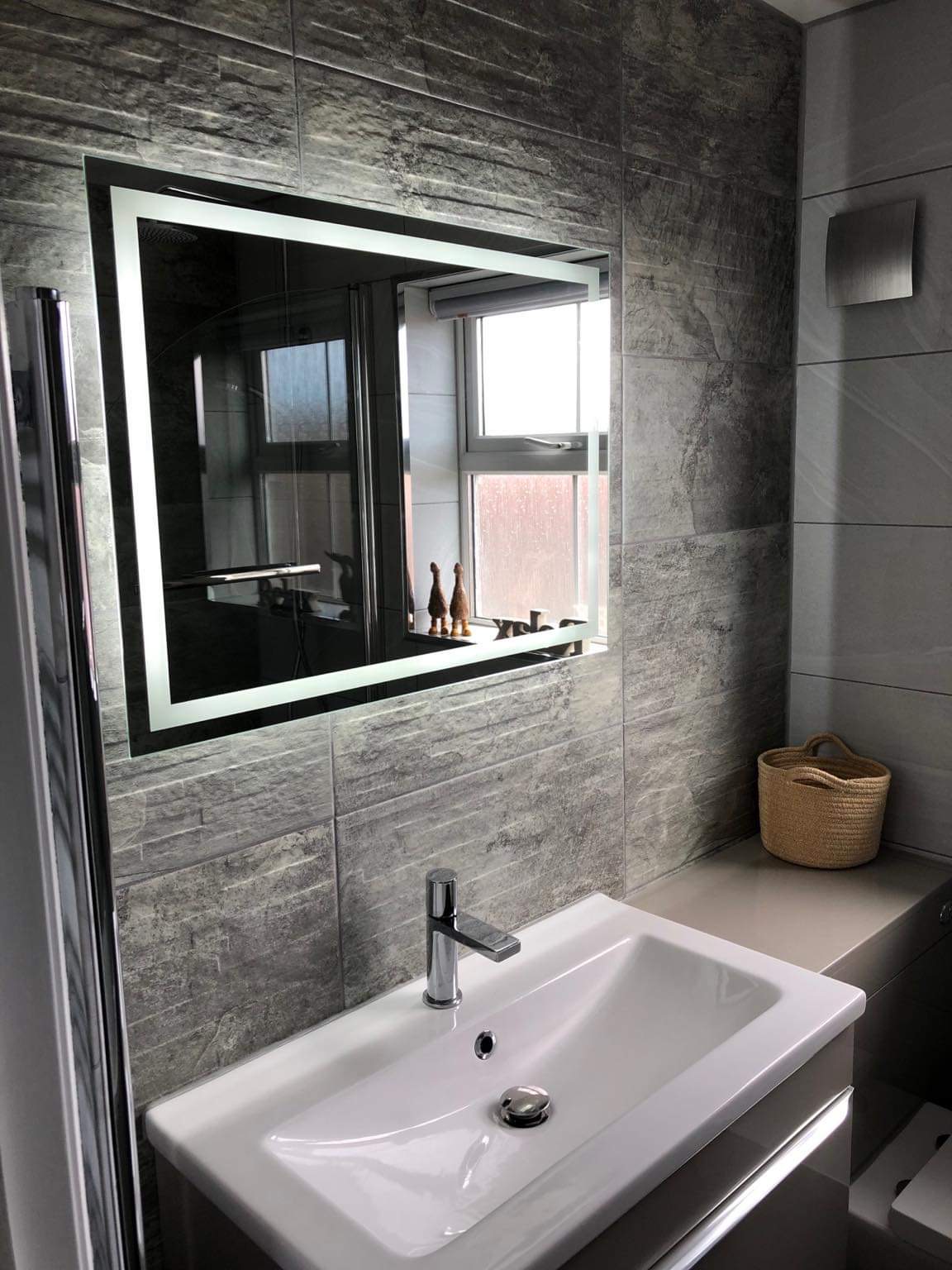 White basin under a large illuminated mirror on textured grey tiles