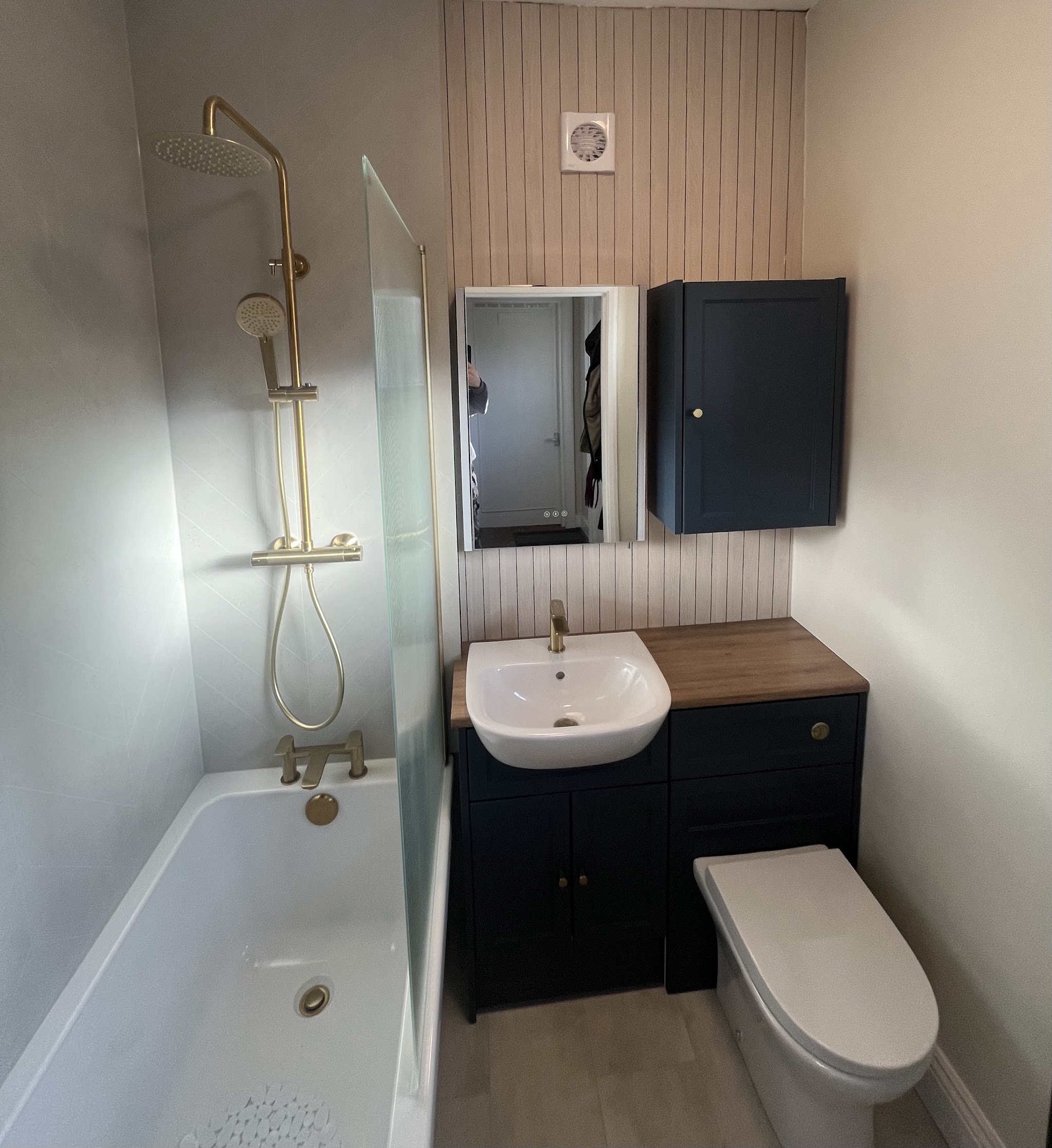 Brushed brass shower over a bath, fluted glass screen and navy shaker furniture with an oak top