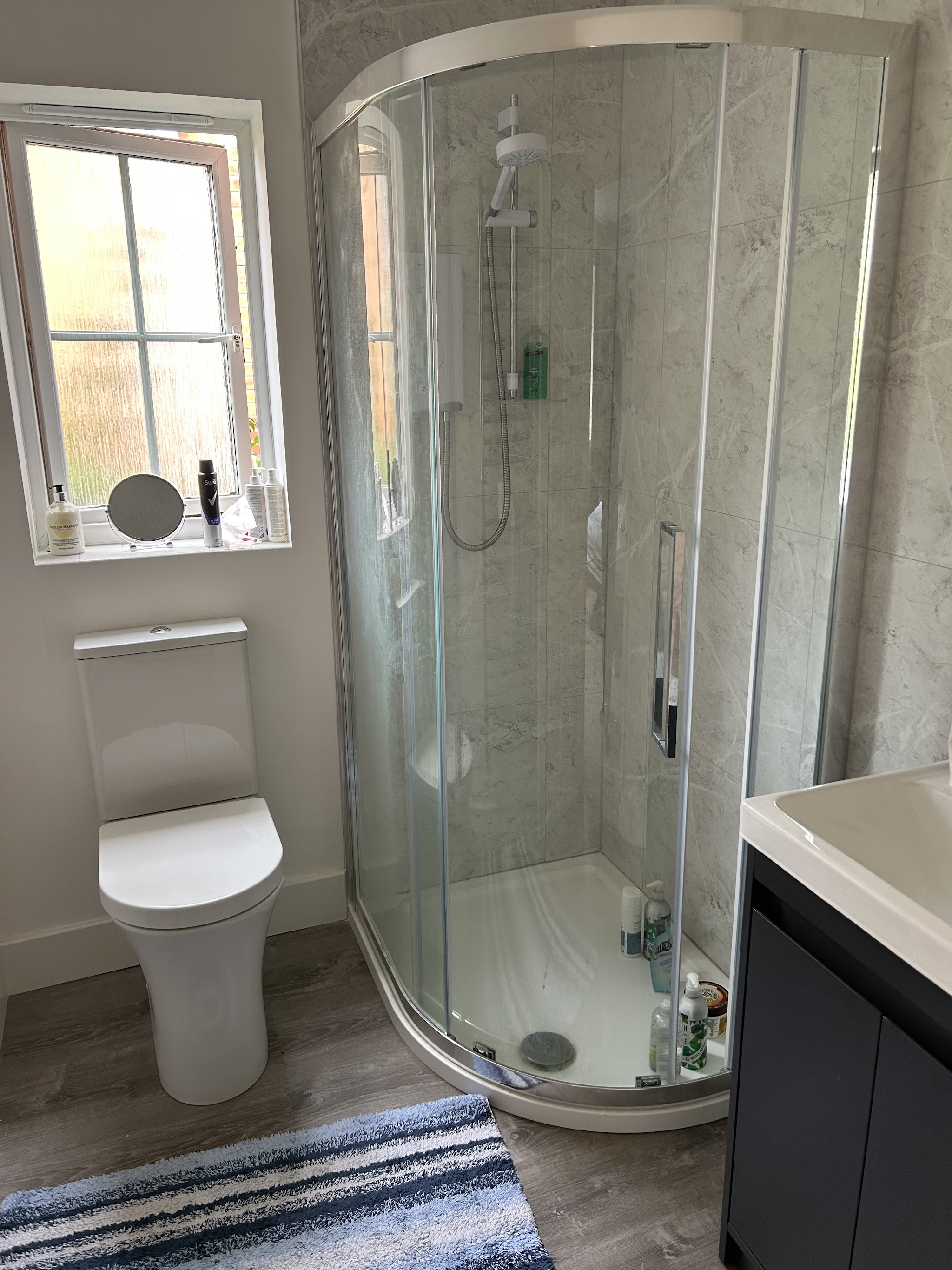 Quadrant shower enclosure with marble-effect wall panels beside a close-coupled toilet